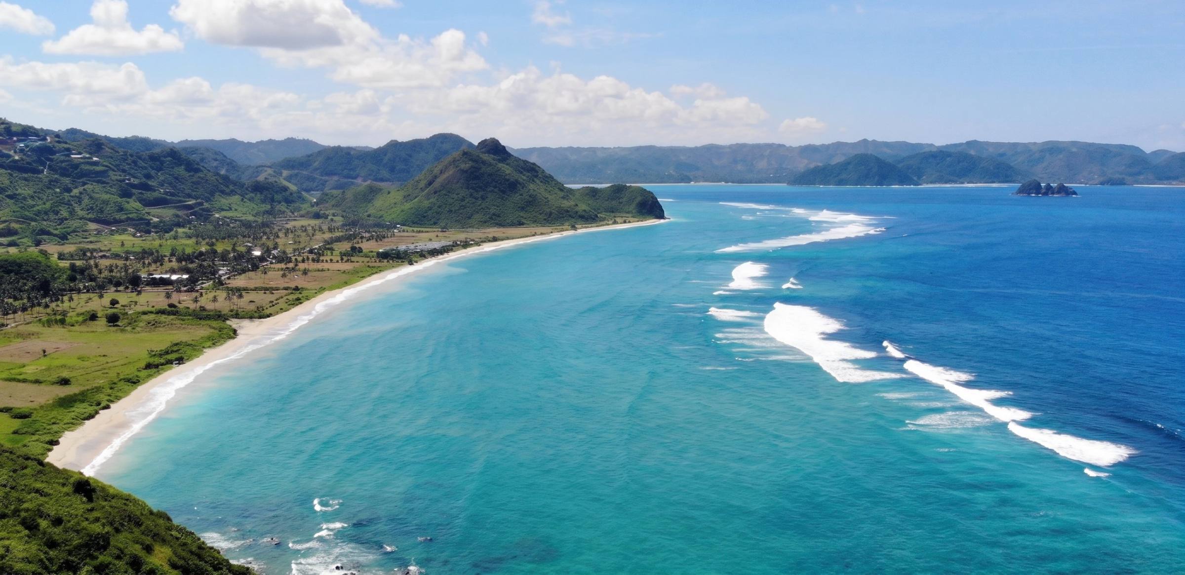 Aerial view of a long white-sand bay, turquoise water and green hills on Lombok's south coast
